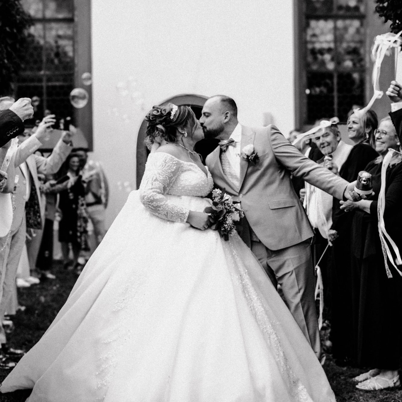 Hochzeitsfotograf Ingelheim Braut und Bräutigam küssen sich, umgeben von feiernden Gästen in eleganter Kleidung.